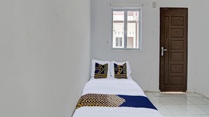 Ein Zimmer mit einem Bett, zwei Kissen mit geometrischem Muster, einem Fenster und einer Tür.