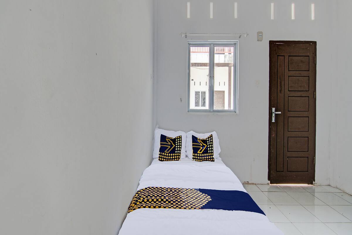 Een kamer met een bed, twee kussens met een geometrisch patroon, een raam en een deur.