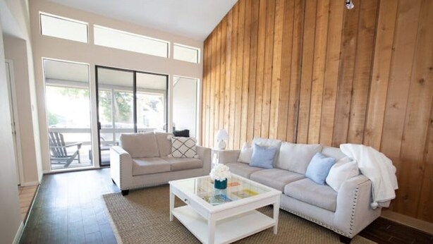 Una sala de estar con un sofá blanco, una mesa de centro de vidrio y una pared de madera.