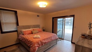 Ein Schlafzimmer mit einem Bett, einem Fenster mit Jalousien, einer Tür, die auf einen Balkon führt, und einem kleinen Schreibtisch mit einer Vase.