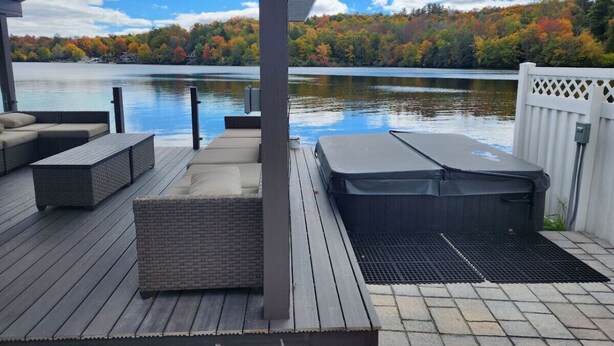Eine überdachte Terrasse mit Sitzgelegenheiten im Freien, einem Whirlpool und Blick auf einen See mit Herbstlaub.