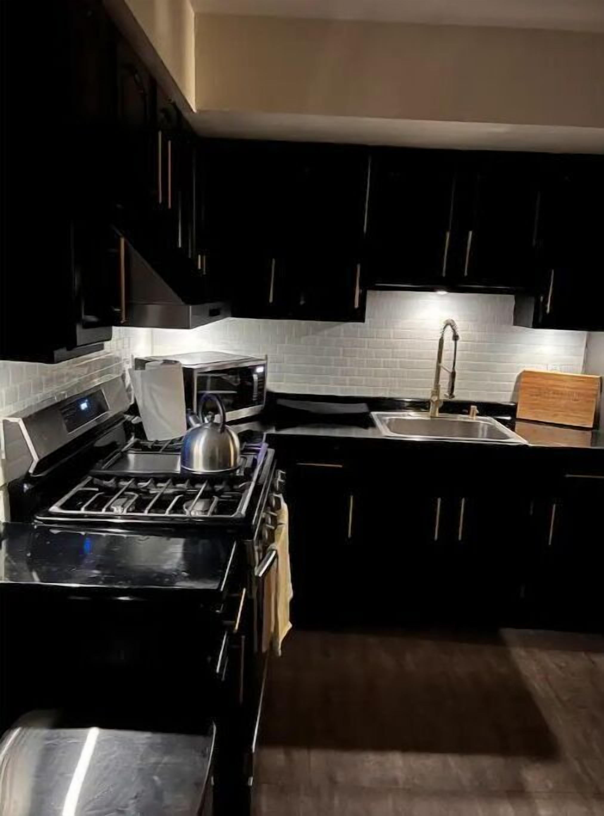 A modern kitchen with dark cabinetry, a stainless steel stove, and a white tiled backsplash.