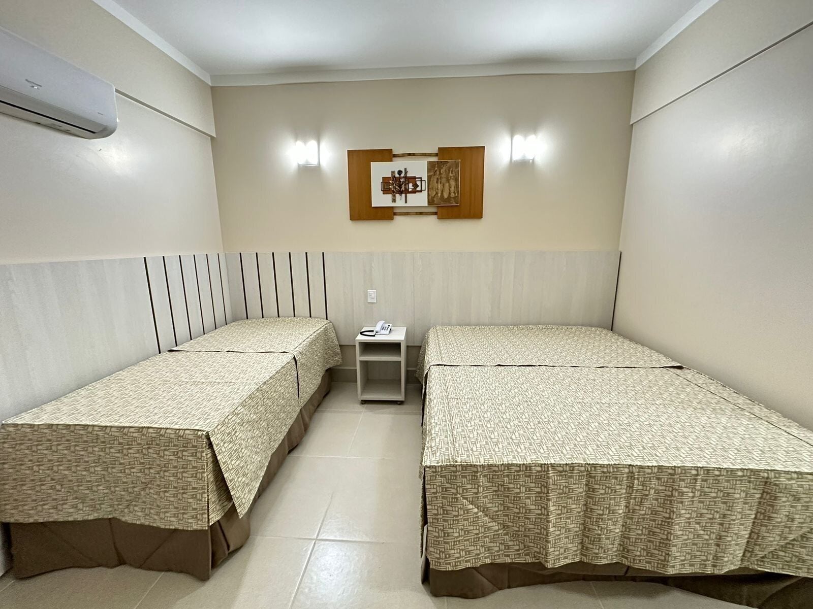 A room with two beds, a small bedside table with a phone, and a wall-mounted light fixture.