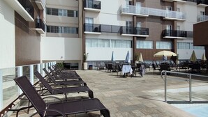 A rooftop terrace with sun loungers, outdoor tables, umbrellas, and a swimming pool. - Di Roma Spazzio Via Caldas (Caldas Novas)