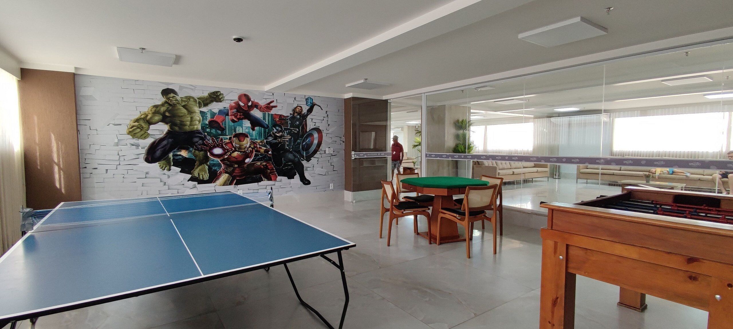 Um quarto com mesa de pingue-pongue, mesa de futebol de mesa e um mural de super-heróis.