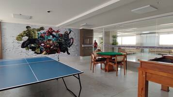 Um quarto com mesa de pingue-pongue, mesa de futebol de mesa e um mural de super-heróis.