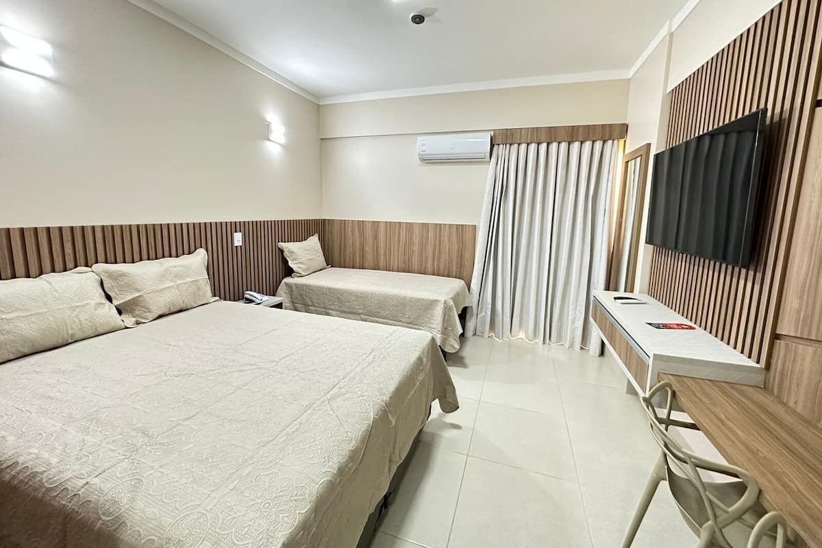 A hotel room with two beds, a desk, a flat-screen TV, an air conditioning unit, and a curtain.