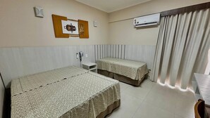 A hotel room with two beds, a bedside table, a telephone, an air conditioning unit, and a window with curtains.