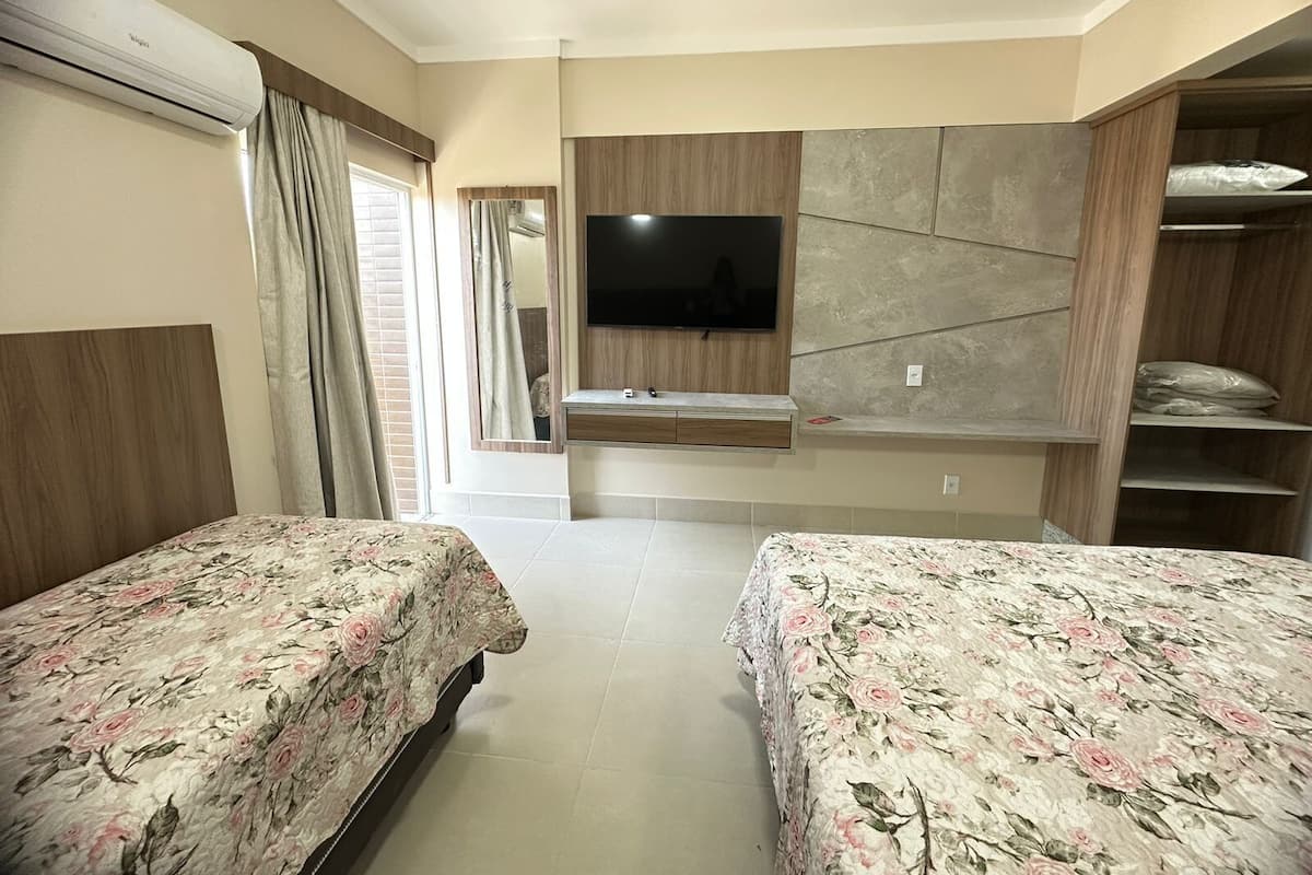 A hotel room with two beds, a TV mounted on the wall, a window with curtains, and a built-in wardrobe.