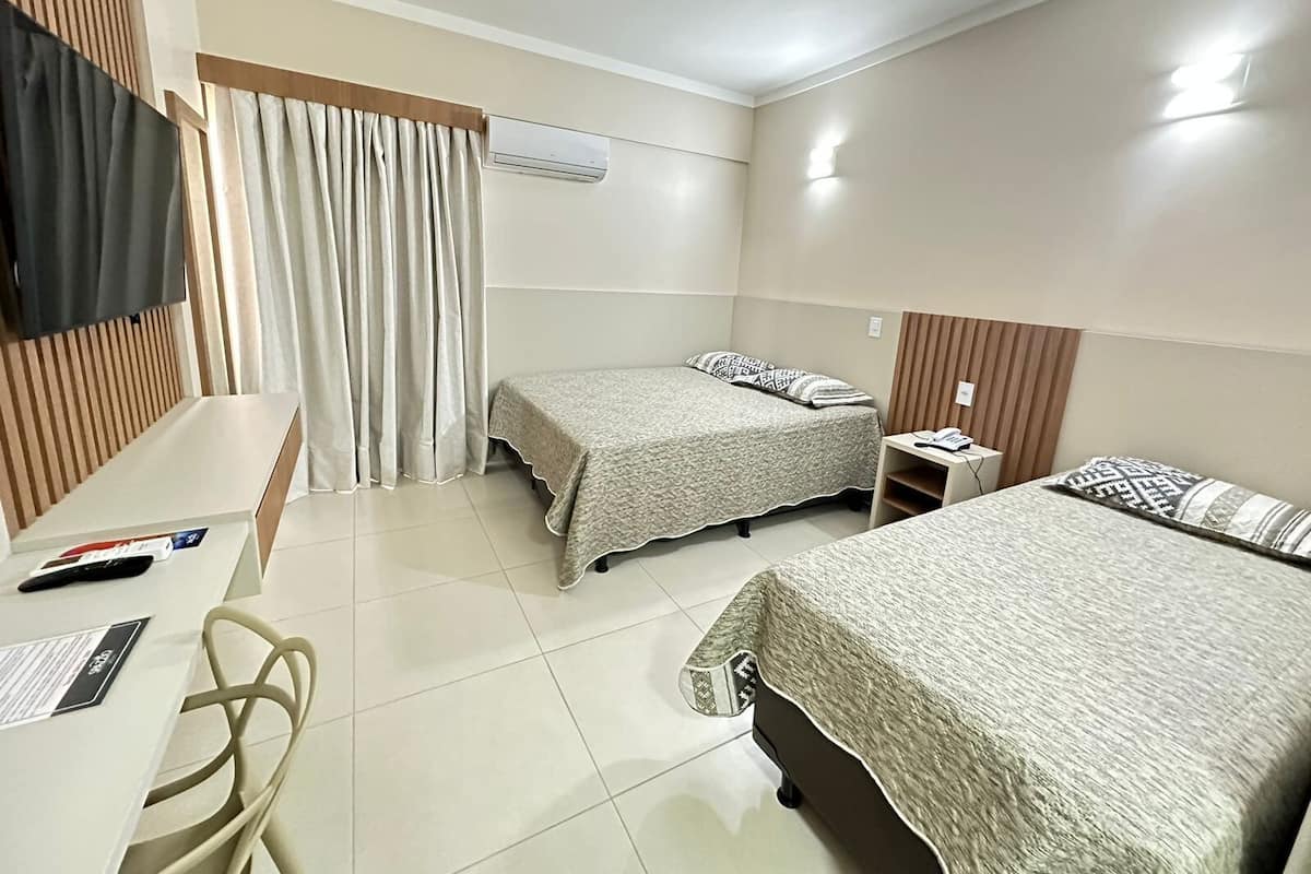 A hotel room with two beds, a desk, a chair, a TV, and an air conditioning unit.