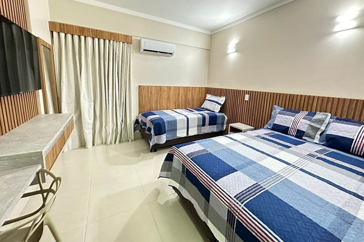 A hotel room with two beds, a desk, a chair, an air conditioning unit, and a window with curtains.