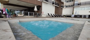 A swimming pool with lounge chairs and a table, surrounded by a building with balconies and windows. - Di Roma Spazzio Via Caldas (Caldas Novas)