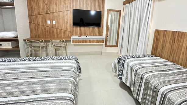Habitació d'hotel amb dos llits, televisió, escriptori amb cadira, mirall i aire condicionat.