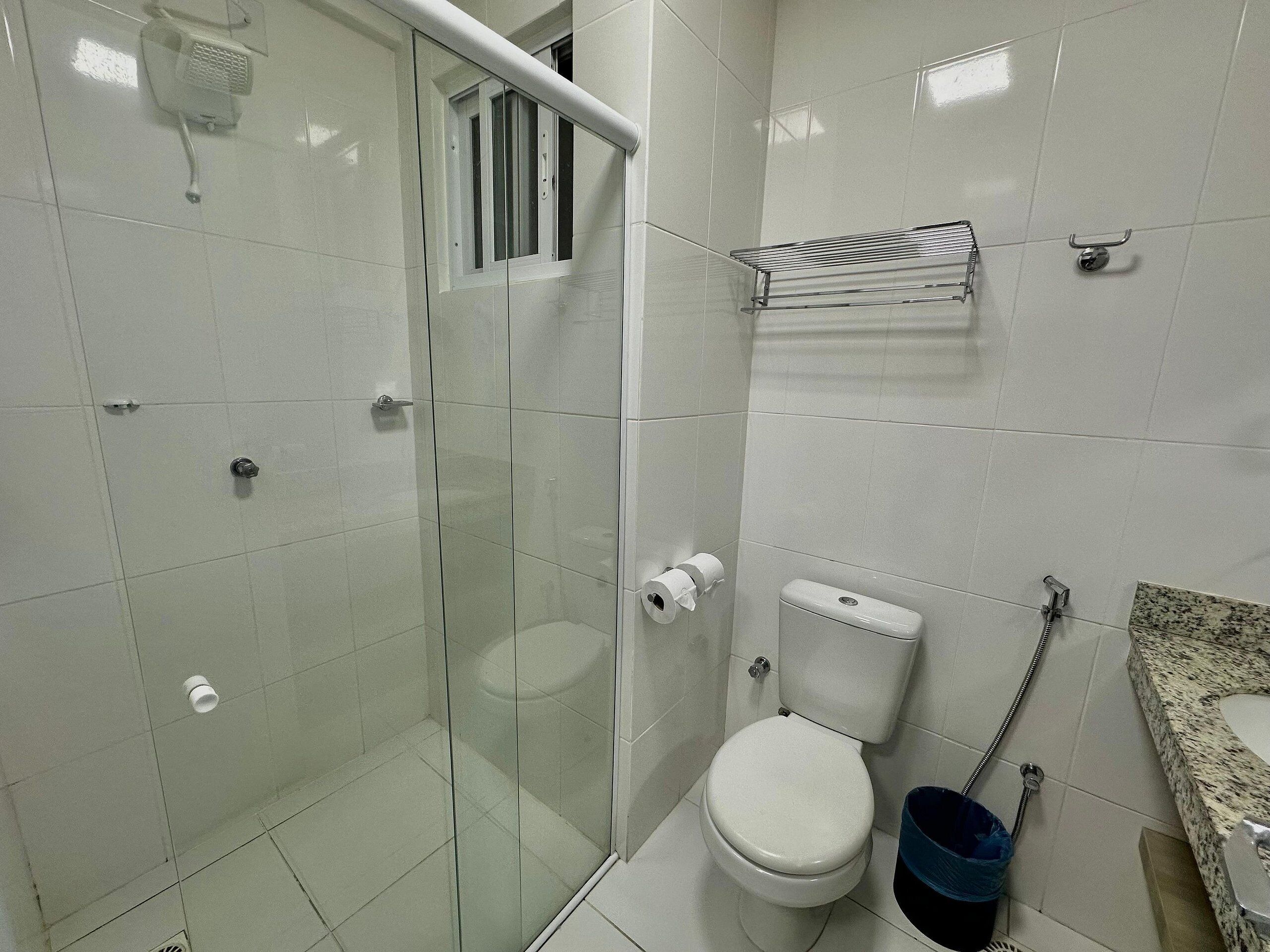 Un baño con ducha de vidrio, inodoro, lavamanos con encimera de granito y perchero para toallas.