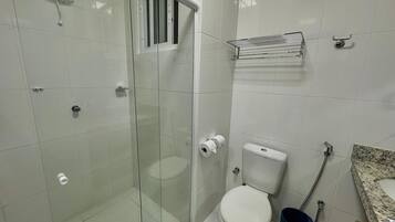 Un baño con ducha de vidrio, inodoro, lavamanos con encimera de granito y perchero para toallas.