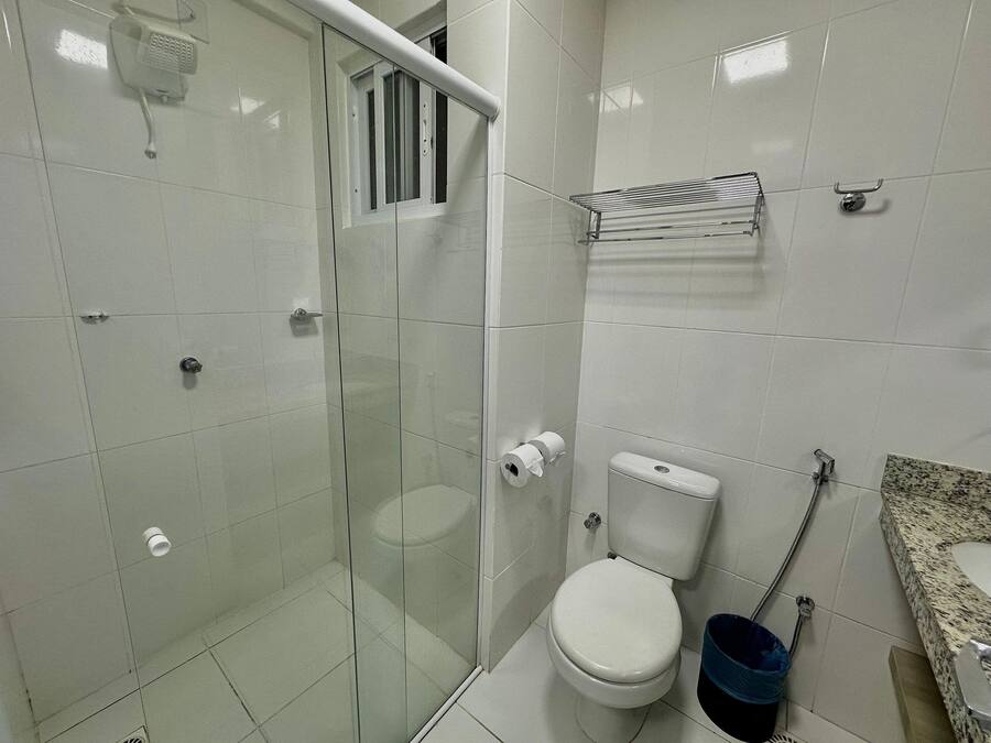 Un baño con ducha de vidrio, inodoro, lavamanos con encimera de granito y perchero para toallas.