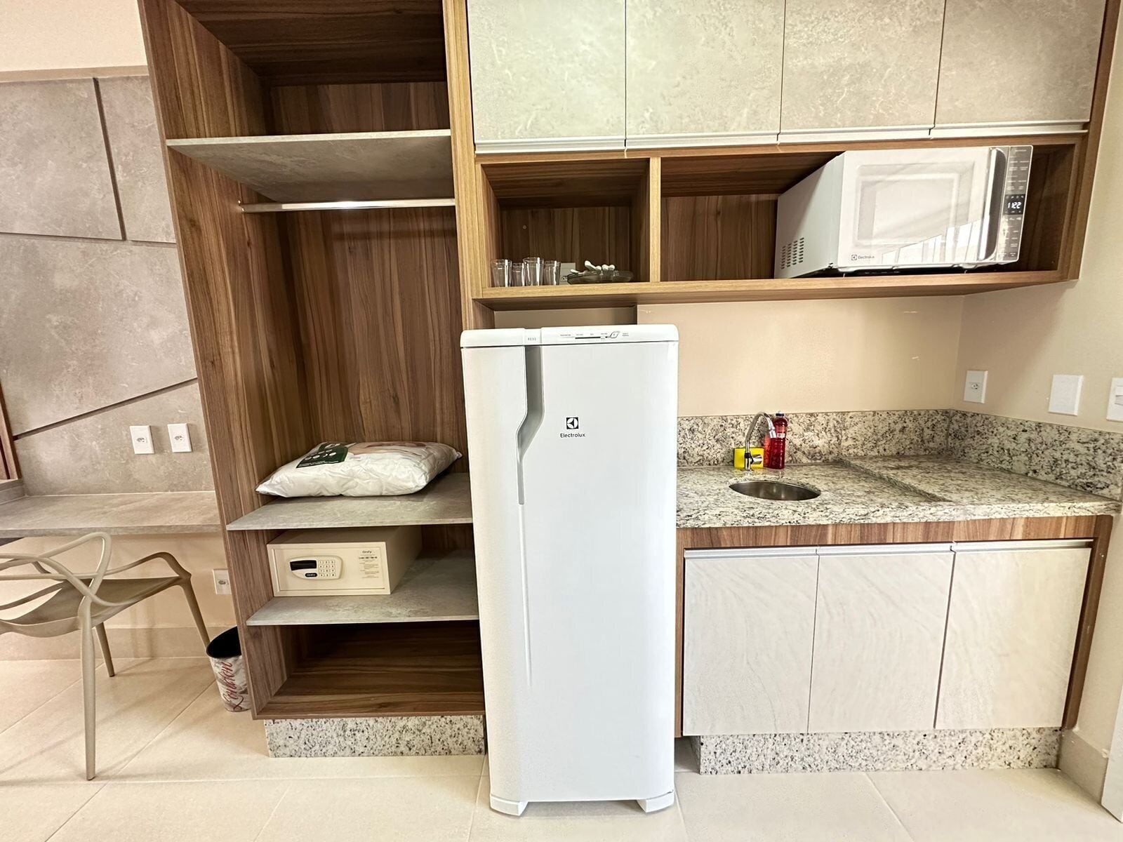 A compact kitchen with a white refrigerator, a microwave, a granite countertop, and wooden cabinetry.