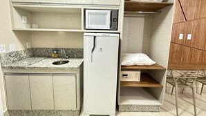 A compact kitchenette with a microwave, refrigerator, granite countertop, sink, and wooden cabinets. - Di Roma Spazzio Via Caldas (Caldas Novas)