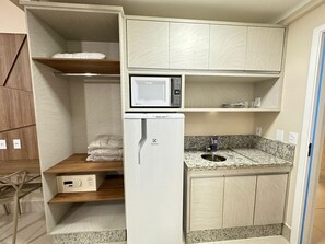Una kitchenette compacta con microondas, refrigerador, encimera de granito y armarios de madera.