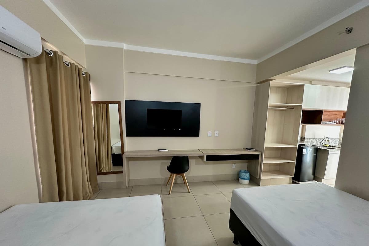 A hotel room with two beds, a desk, a TV, and a kitchenette.