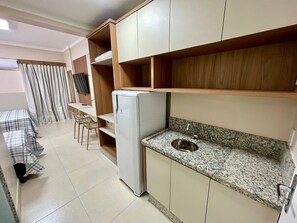 A compact kitchen with a built-in refrigerator, a granite countertop, and a sink. - Di Roma Spazzio Via Caldas (Caldas Novas)