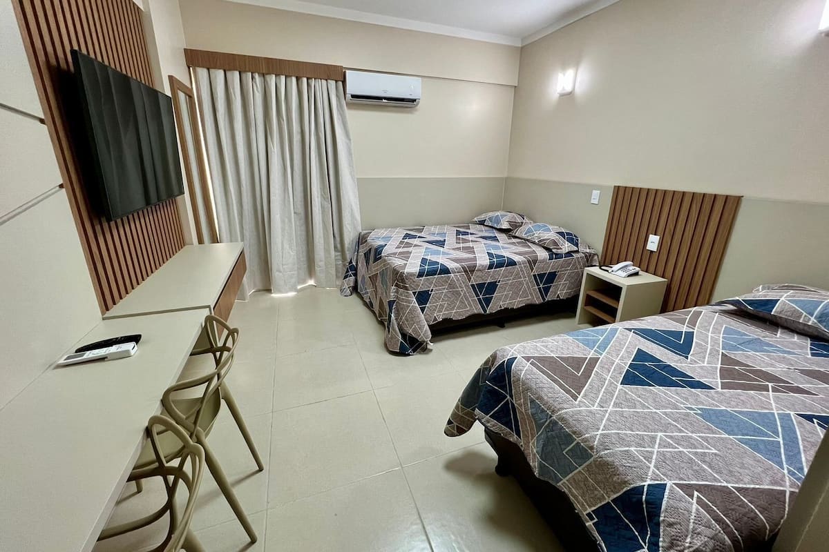 A hotel room with two beds, a desk, a chair, an air conditioning unit, and a television.