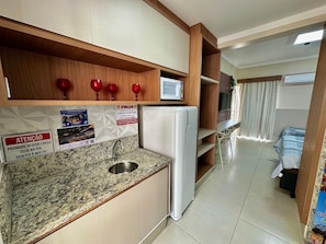 A compact kitchen with a refrigerator, a sink, and wooden shelves. - Di Roma Spazzio Via Caldas (Caldas Novas)