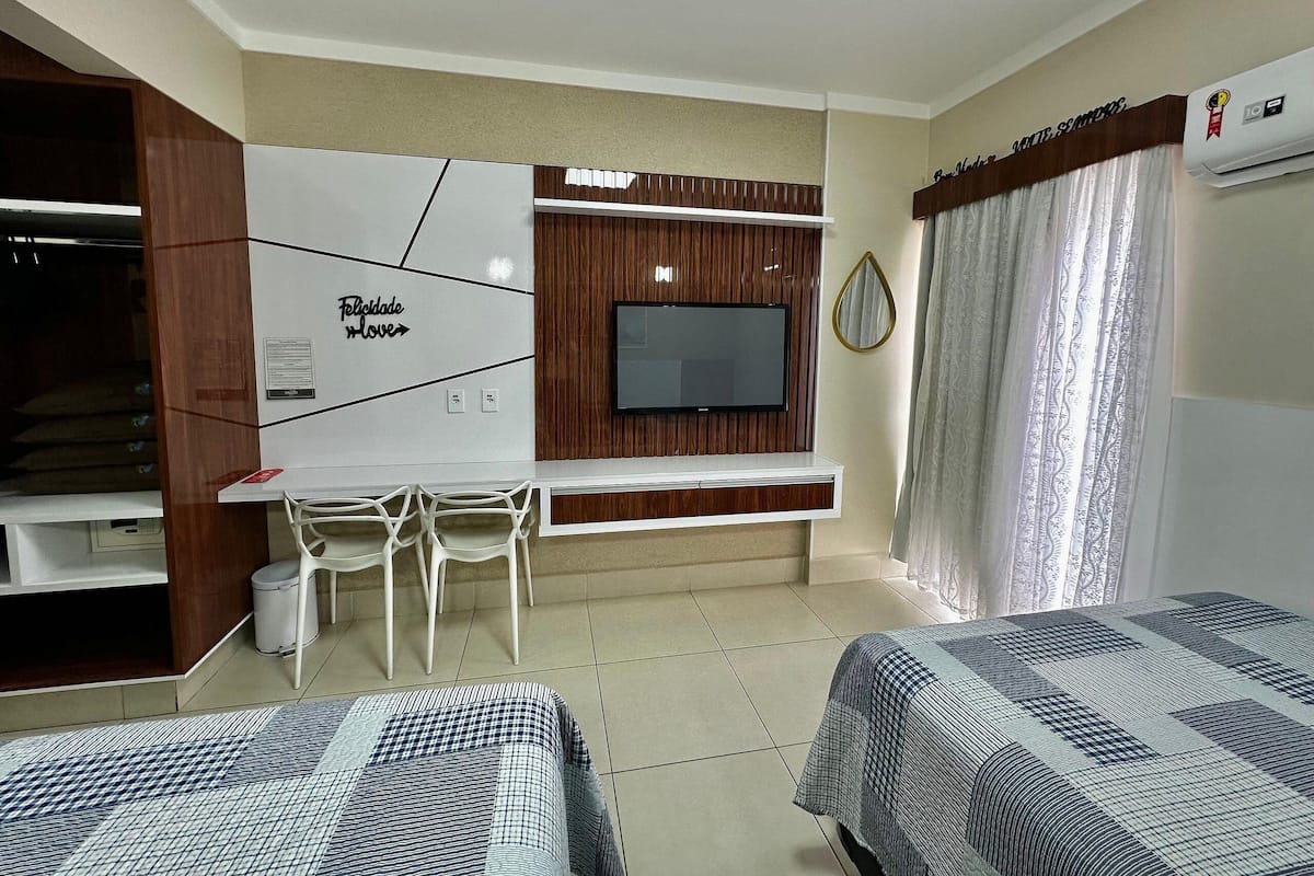 A hotel room with a TV, a desk, two beds, and a wardrobe.