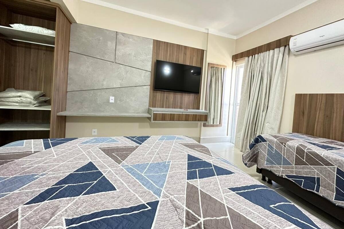 A hotel room with a large bed, a TV mounted on the wall, a wardrobe, and an air conditioning unit.