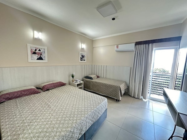 Ett hotellrum med två sängar, ett skrivbord, ett fönster med gardiner och en taklampa.