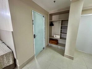 A room with a closed door, a bed with a patterned bedspread, a closet with shelves and a folded blanket, and a small box on the floor. - Di Roma Spazzio Via Caldas (Caldas Novas)