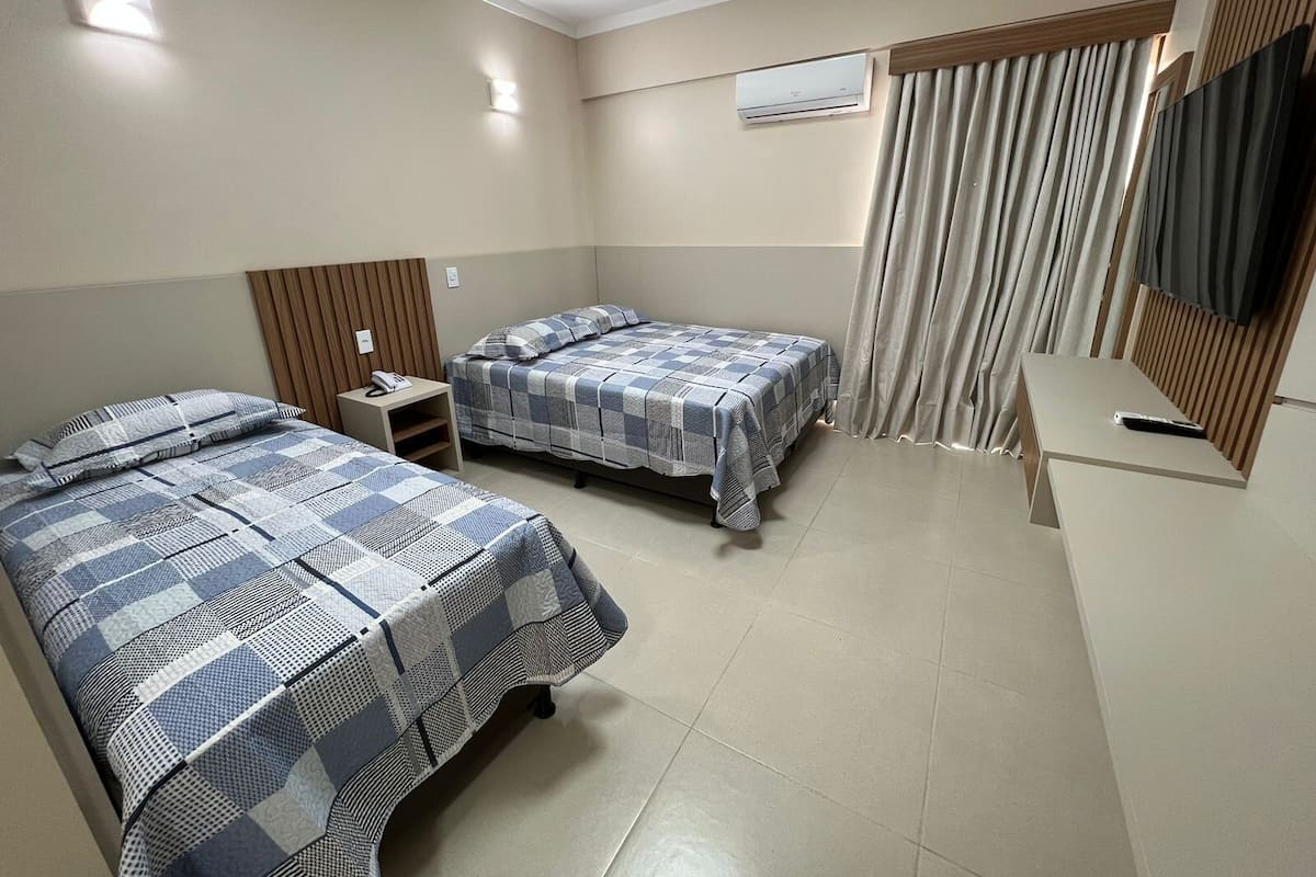 A hotel room with two beds, a small table, a TV, and an air conditioning unit.