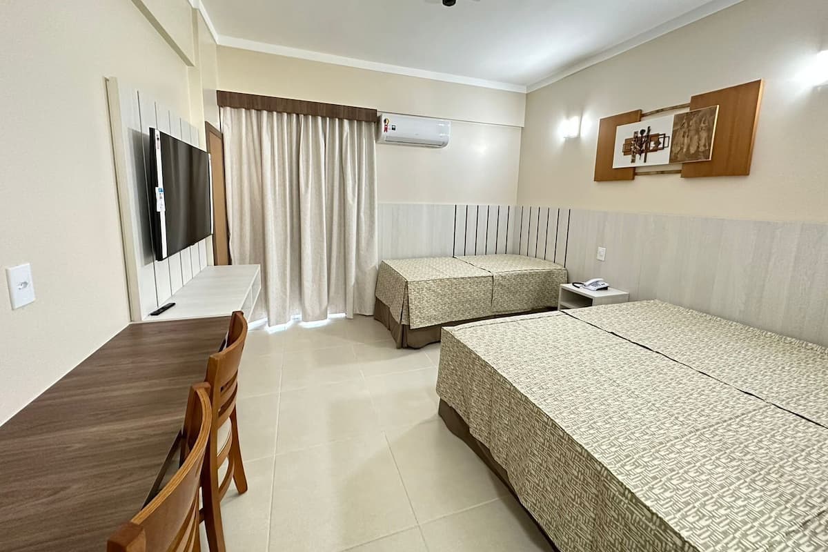 A hotel room with a bed, a desk, a chair, a TV, a bedside table, and curtains.