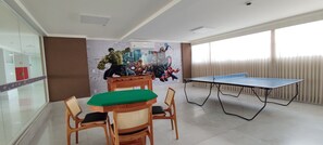 A room with a ping pong table, wooden chairs, a green table, and a wall mural. - Di Roma Spazzio Via Caldas (Caldas Novas)
