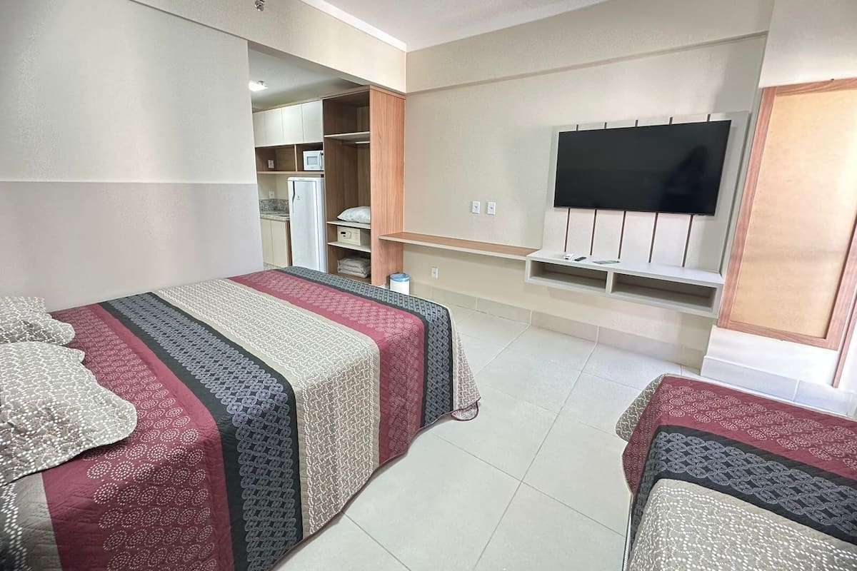 A hotel room with two beds, a TV, a kitchenette, and a wardrobe.