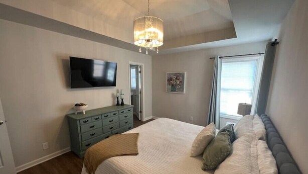 Une chambre avec un grand lit, une commode, une télévision et une fenêtre.