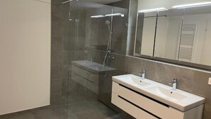 Un bagno moderno con doccia vetrata, doppio lavabo e un ampio specchio.