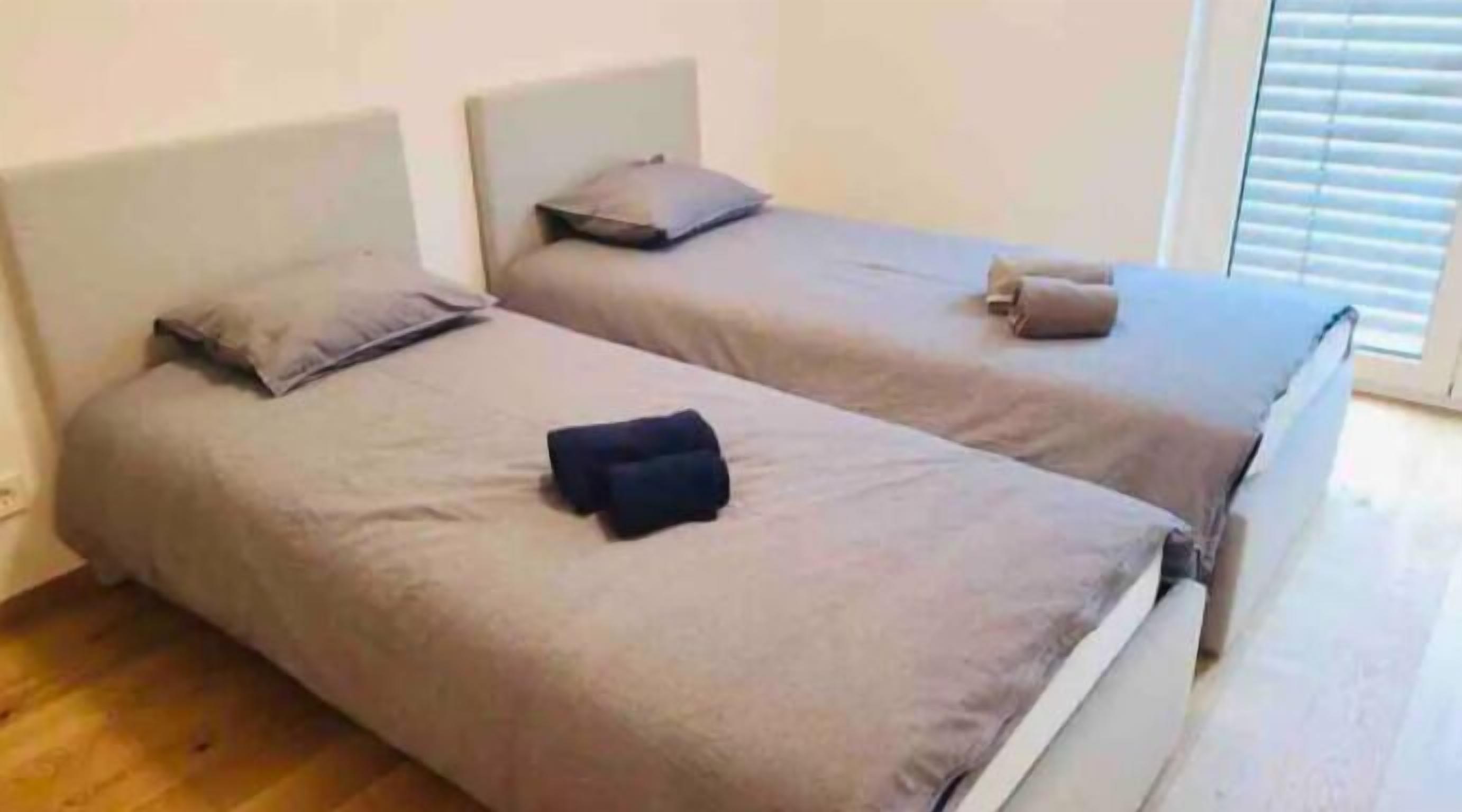 Quarto com duas camas de solteiro, cada uma com travesseiro e cobertor.
