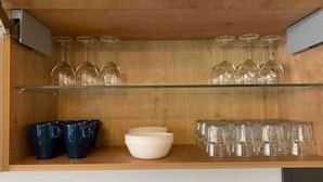 Uno scaffale in legno con bicchieri da vino, ciotole e tazze.