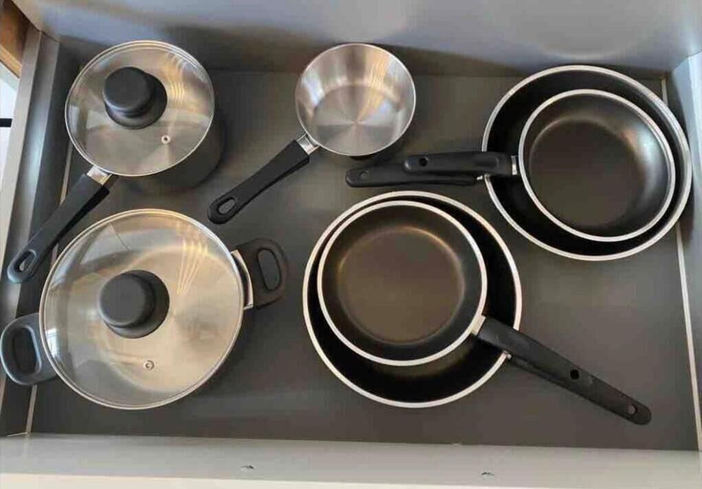 A kitchen with a stove, pots, pans, and a frying pan.