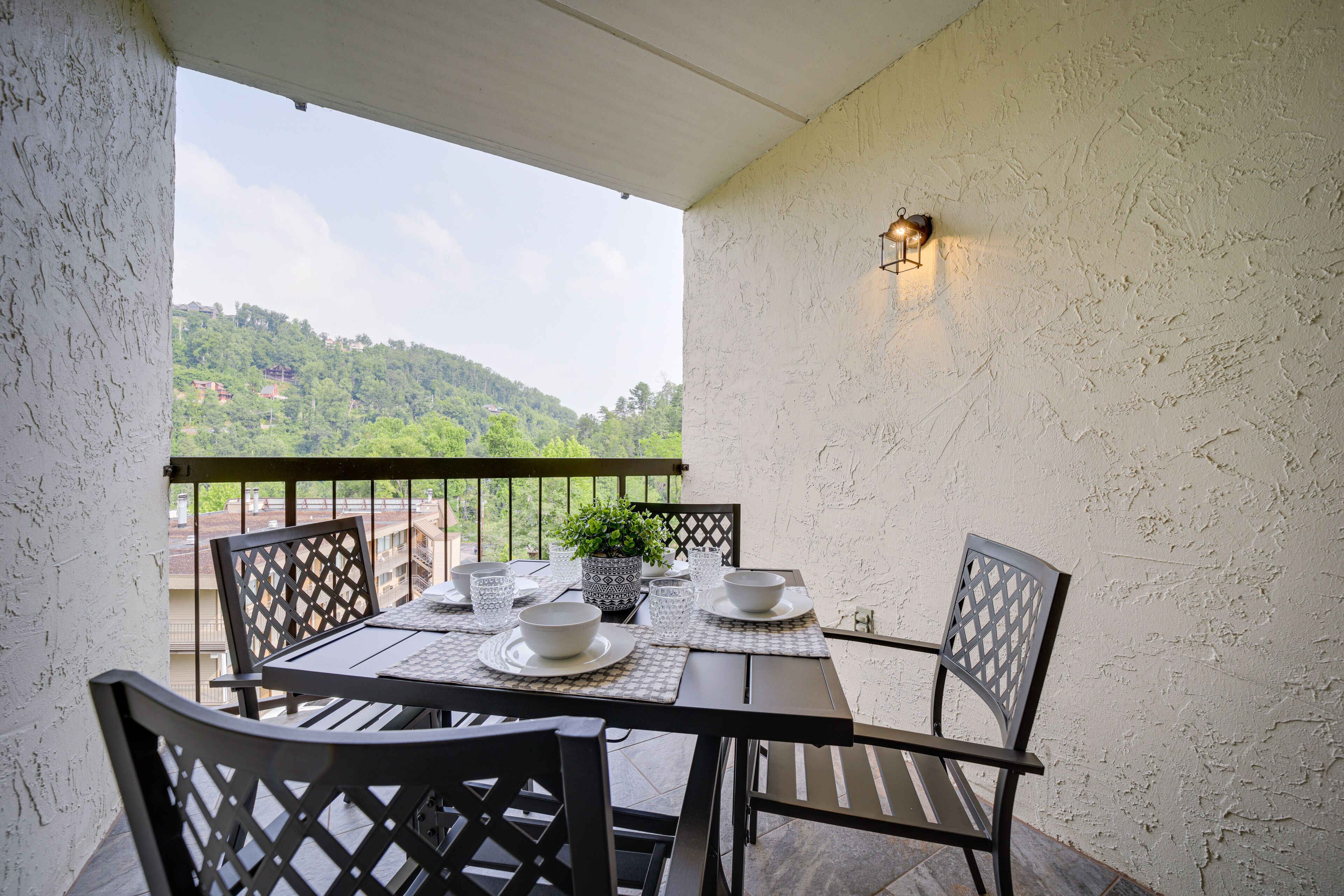En balkon med et spisebord, stole, en potteplante og en vægmonteret lampe.