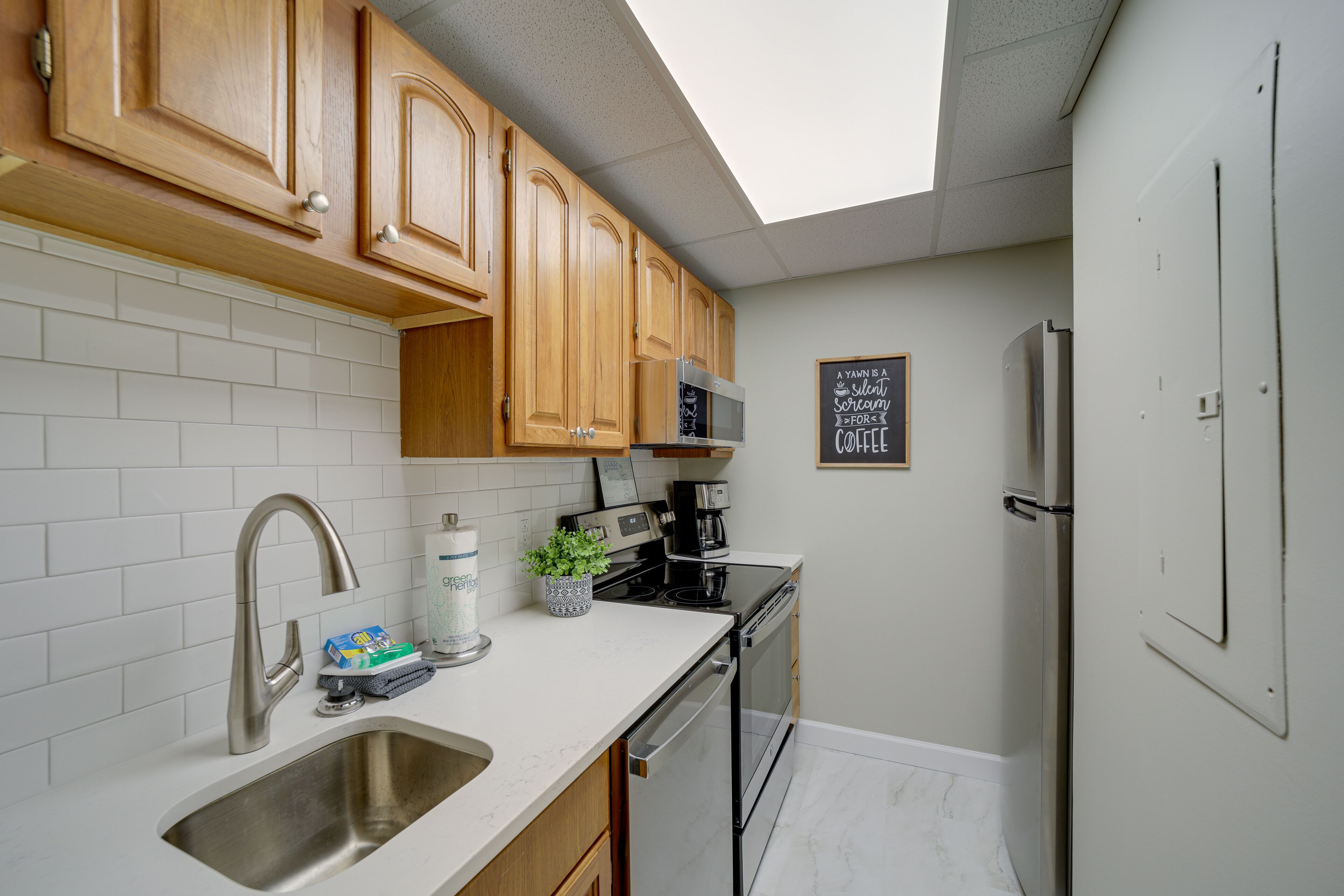 A compact kitchen with wooden cabinets, a stainless steel sink, a microwave, and a refrigerator.