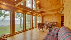 A wooden cabin with large windows, a sofa, and a dining area. - Lake Champlain Vacation Rental with Boat Dock! (St. Albans Town)
