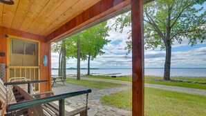 A wooden cabin with a porch, a bench, and a view of a lake. - Lake Champlain Vacation Rental with Boat Dock! (St. Albans Town)