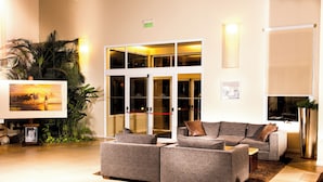 Un hall d’entrée moderne avec un canapé d’angle gris, un grand tableau encadré et une plante en pot.