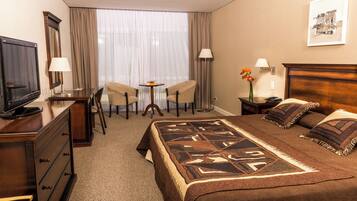 A hotel room with a bed, a TV, a desk, two chairs, a small table, and a window with curtains.