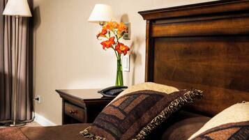 A neatly made bed with a brown headboard, a bedside table with a lamp and a vase of flowers, and a wall-mounted light fixture.
