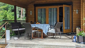 Un espace extérieur abrité, doté d’une table et de chaises, d’une terrasse en bois et d’une porte donnant sur l’intérieur.