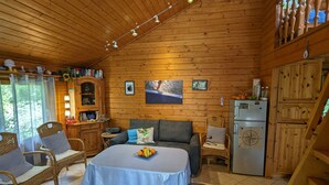 L’intérieur d’un chalet en bois accueillant, avec une table à manger, des chaises, un canapé, un réfrigérateur et une bibliothèque.