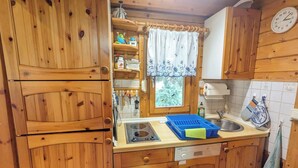 Une cuisine en bois équipée d’un lave-vaisselle Siemens, une fenêtre avec un rideau et une horloge au mur.